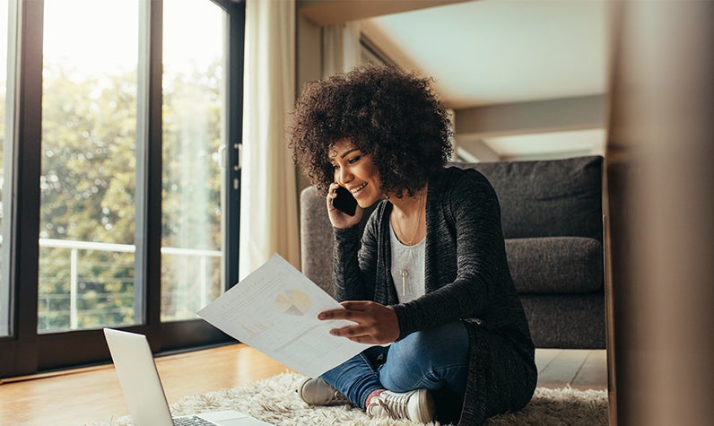 A woman surveying financial information while sitting on the floor of her new home.