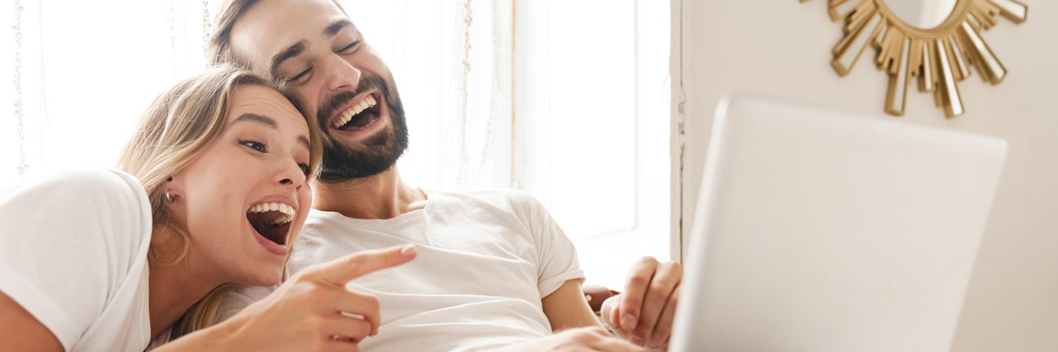 A couple looks at a computer screen and laughs.