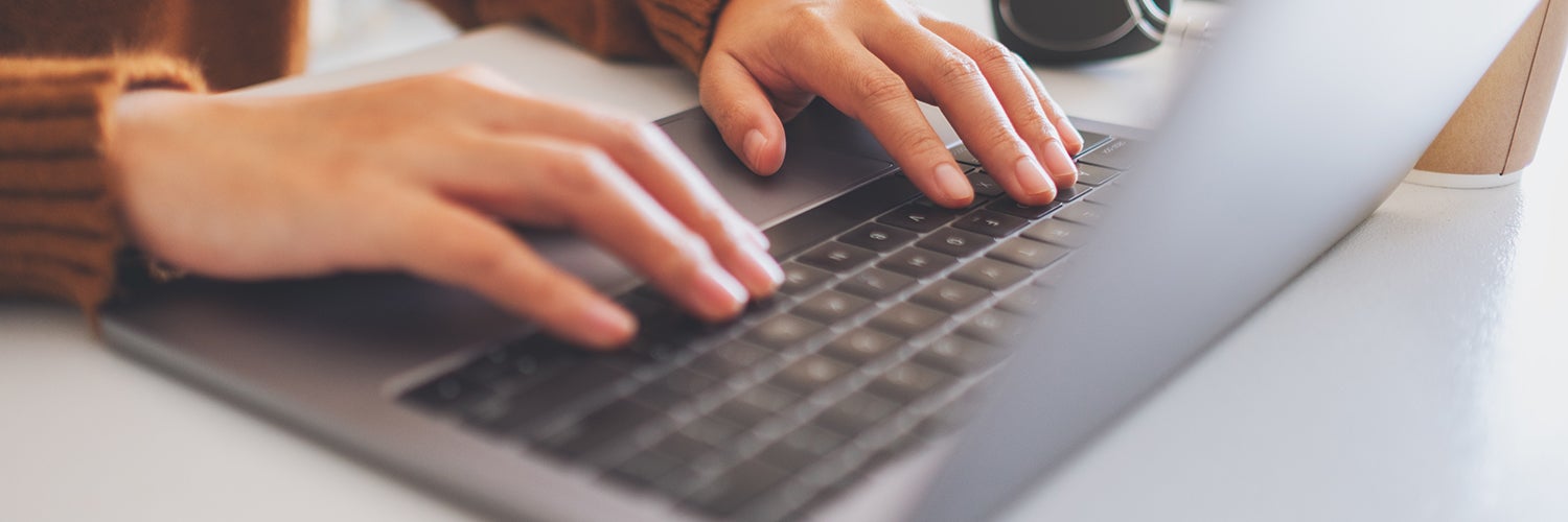 A person's hands typing on a laptop keyboard.