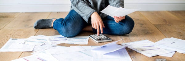 person wearing a long sleeved stripped shirt sitting on the ground and using a budget calculator to figure out their finances