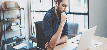 man sits at desk looking at laptop